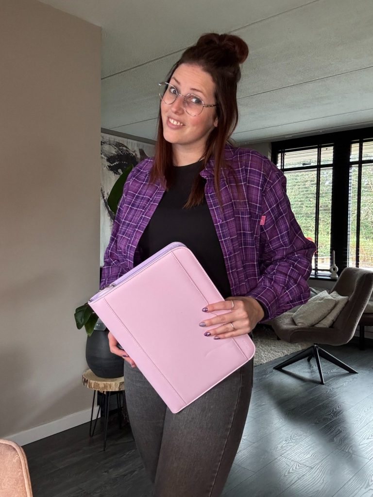 Jonge vrouw interieurstylist met bril houdt een tas vast, gekleed in een bloemenprint en een jeansjack.