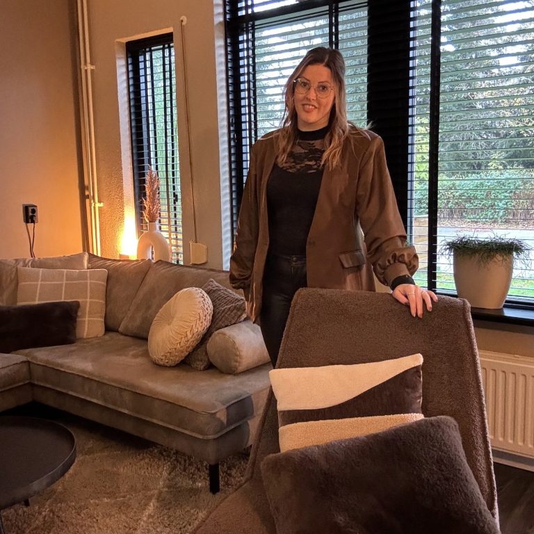 Een vrouw met een paarse trui zit aan een tafel met een kleurenschema en een vaas met tulpen.