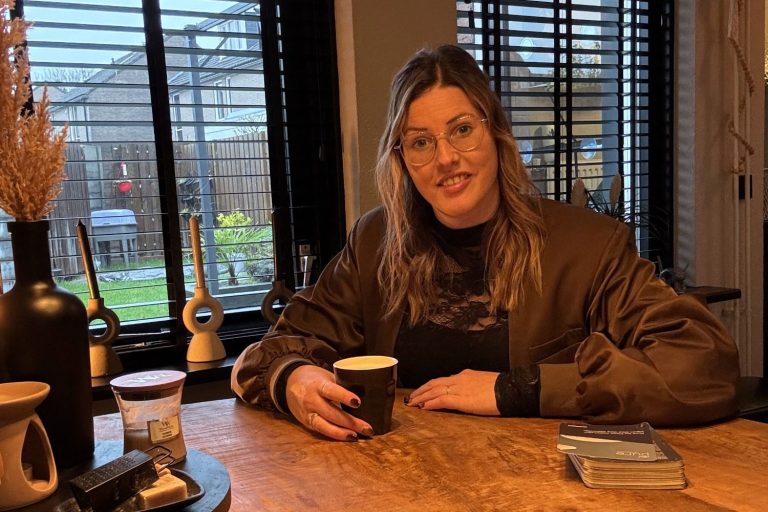 Een vrouw met een spijkerjasje schrijft iets op papier aan een bureau bij kvk.